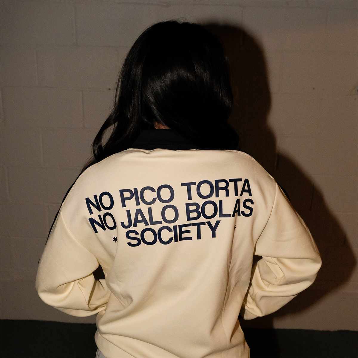 Model seen from behind wearing the No Pico Torta Society cream jacket by Caracas Merch